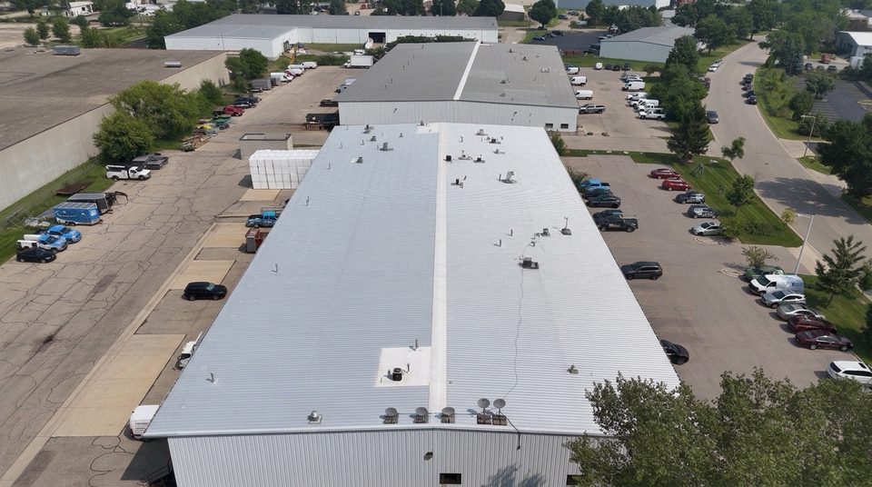 Before: aerial view of a weathered gray metal warehouse roof in Wisconsin with worn seams and rooftop units