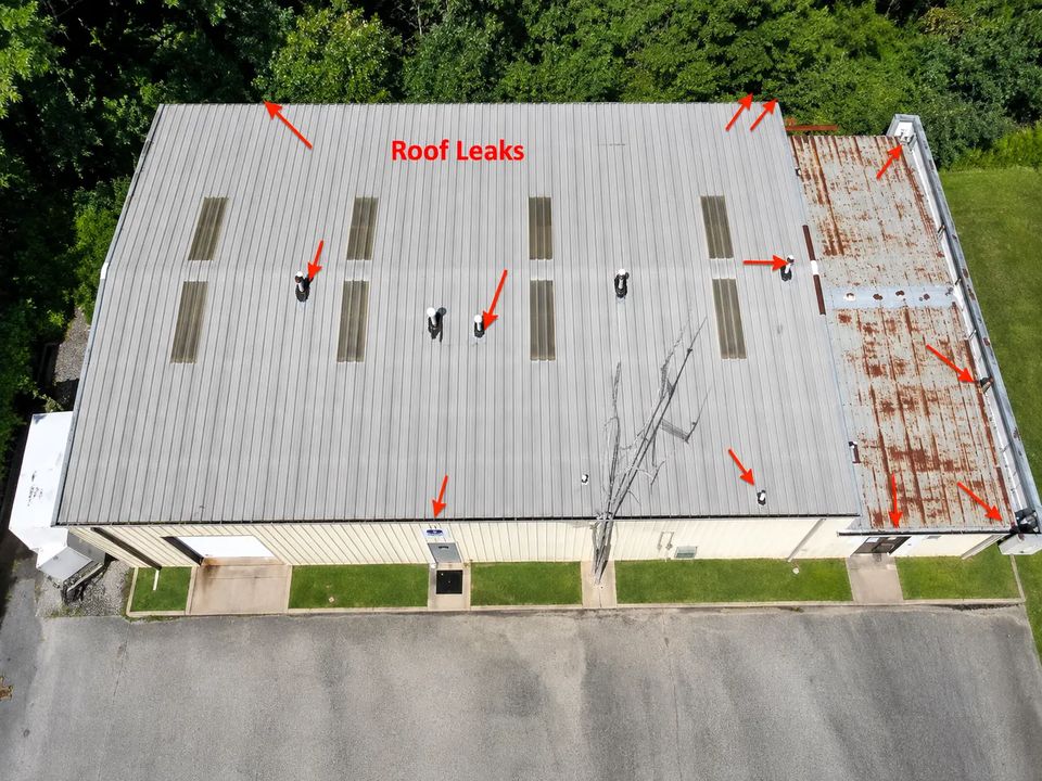 Before: aerial view of a commercial metal roof in Bloomington, Indiana with rusted panels, worn seams, and active roof leaks marked around vents and curbs
